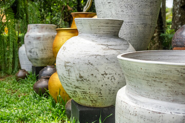 Fototapeta premium Close up of large handcrafted ceramic pots in white and gold tones displayed in tropical garden in Phuket, Thailand. Traditional Thai craftsmanship. Artisan craftsmanship and Traditional pottery