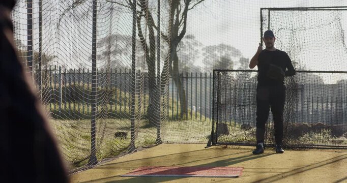 Catcher signaling pitcher executing windup and throwing baseball in batting cage to refine accuracy