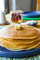 Homemade family breakfast with pancakes and honey on rustic table Description: Top view of a family breakfast table with freshly cooked pancakes stacked on a blue plate, topped with butter and served