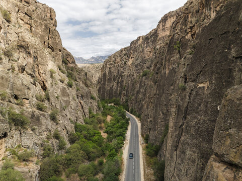 Aerial view of a winding road cutting through the rugged, sun-kissed cliffs of the canyon, a solitary car navigating the path, Magellan cave, Vayots Dzor Province, Armenia.