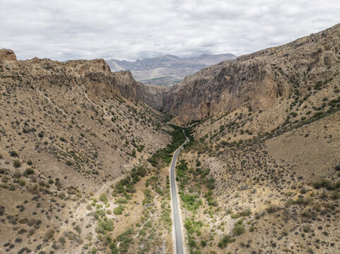 Aerial view of a road winding through a deep canyon under a cloudy sky, between rugged mountains, Magellan cave, Vayots Dzor Province, Armenia.