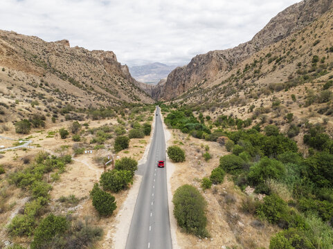 Aerial view of a striking red car navigates the long road through a dramatic canyon landscape, Magellan cave, Vayots Dzor Province, Armenia.