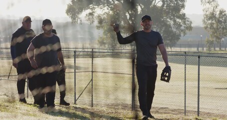 Joining from left, diverse male teammates walking on slope past fence with gloves preparing defense