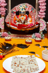 Nut Barfi Offering on Plate with Krishna Idol in Background.