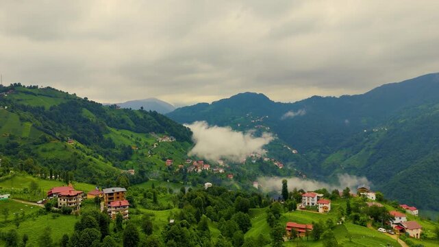 Low clouds covering the green hills and tea plantations surrounding a mosque and traditional houses in Camlihemin valley, Rize province, Black Sea region, Turkiye