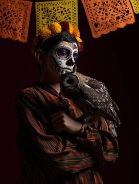 Boy dressed as a catrin for the Day of the Dead with a serious and proud look, holding his arm up for his owl to rise. He wears face makeup and a flower crown. Paper banners hang.