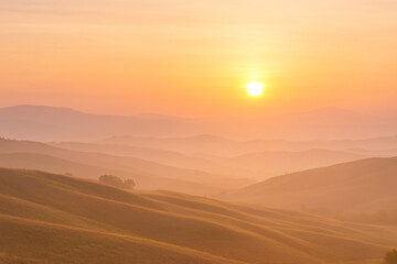 Obraz premium Peaceful Sunrise Landscape with Rolling Hills in Yellow and Pink Light