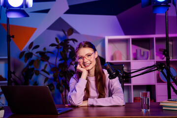 Confident blogger in modern studio recording podcast with microphone and laptop