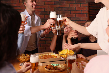Group of happy friends clinking glasses of beer at table indoors