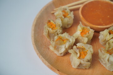 delicious steamed dumplings served on a wooden plate with dipping sauce and chopsticks