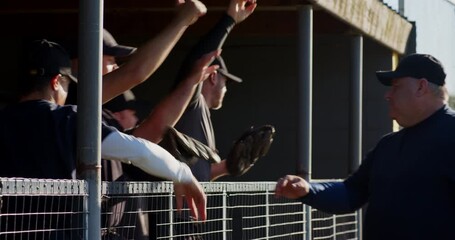 Coach approaching male baseball players at dugout fist bumping before jogging for warmup - Powered by Adobe