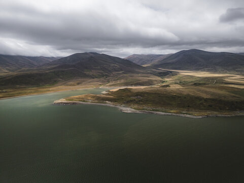 Aerial view of the tranquil Spandarian Reservoir reflecting the overcast sky, nestled amidst rolling hills and rugged mountains, Spandarian Reservoir, Syunik, Armenia.