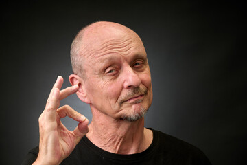 Closeup portrait of a elderly man in studio doying the sign for perfect