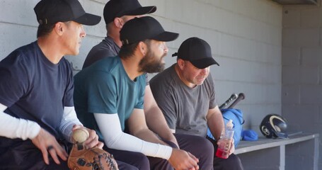 Diverse male teammates waiting innings in dugout, passing baseball and pointing at field to discuss