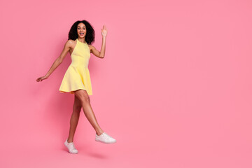 Joyful young woman in yellow dress smiling and waving against pink background, promoting lifestyle and summer fashion