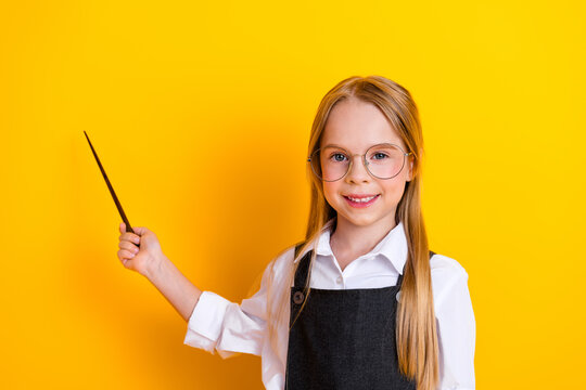 Smiling schoolgirl with glasses holds pointer and poses against vibrant yellow background embodying education and joy - Powered by Adobe