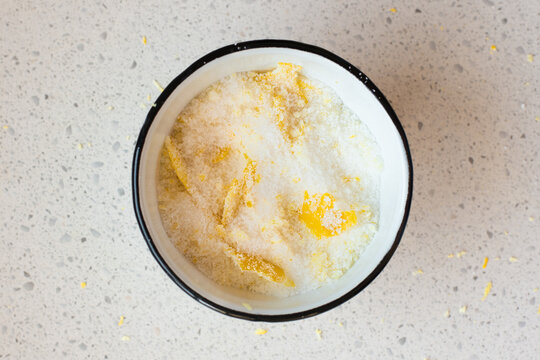 a white enamel bowl has lemon peels in sugar.