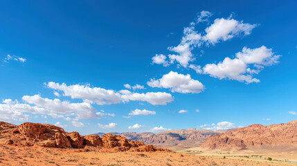 Fototapeta premium Stunning panoramic view of desert landscape featuring red rock formations, blue sky, and fluffy white clouds, evoking sense of tranquility