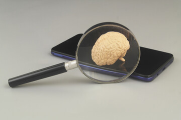 Smartphone with human brain under magnifying glass.	