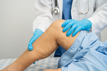 Doctor checking Asian elderly woman patient with scar knee replacement surgery in hospital.