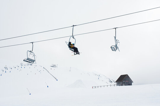 Skiers on ski lift with cabin and snowy mountain in background