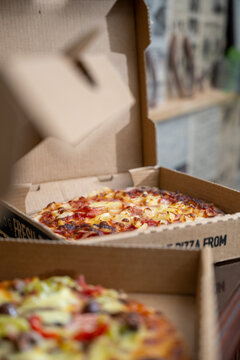 Two open pizza boxes placed on a dark tabletop surface
