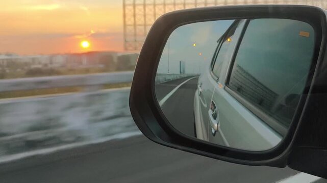 A first&mdash;person view of the car through the side mirror, which reflects the highway and sunset, fences, glowing roadside lights and blurred images are visible - cinematic shots of travel and lifestyle.
