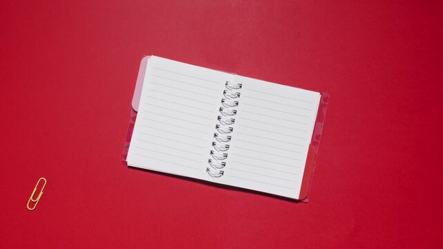 Stationery cycles around a spiral notebook with copy space on red background, loopable stop motion animation