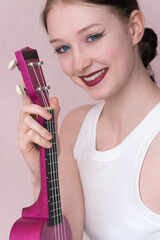 Closeup of beaming young female musician got ukulele in hand, looking straight at camera with big smile, radiant expression that says she's feeling inspired. Caucasian woman, aged 18, true inspiration