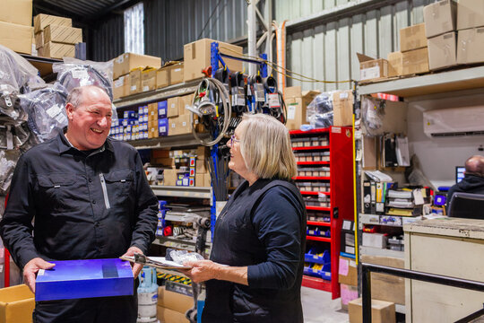 Parts person in mechanics workshop talking with woman customer about spare vehicle supplies