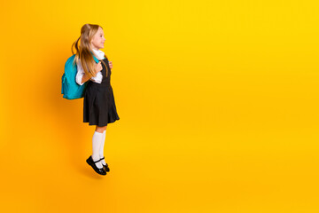 Smiling young schoolgirl in uniform with backpack standing on yellow background ready for a new school year