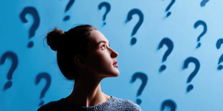 Thoughtful young woman in blue shirt stands against blue background with floating question marks, symbolizing decision-making, confusion, or curiosity.