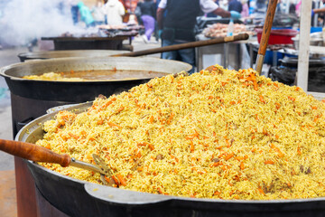 A large cauldron with a huge pile of traditional pilaf at a bustling outdoor street food festival