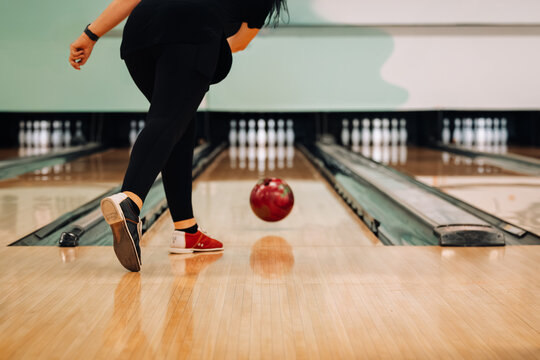 Woman rolling red ball down lane towards pins at a 10 pin bowling alley