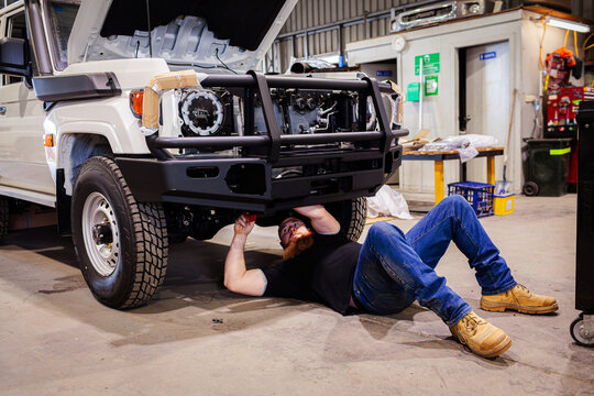 mechanic working under new vehicle installing new bulbar in workshop