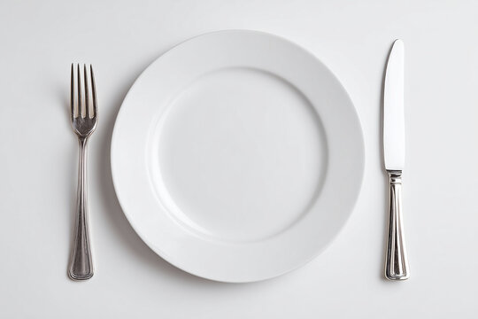Empty white plate with silver fork and knife on a white background, minimal table setting for dining or meal preparation.