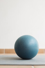 Close-up of a single small blue fitness ball on a yoga mat in a bright minimalist room with soft natural light, symbolizing balance, simplicity, and wellness in a healthy lifestyle setting