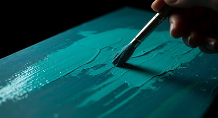 Close-up of a paintbrush applying thick teal paint to a surface with textured strokes.