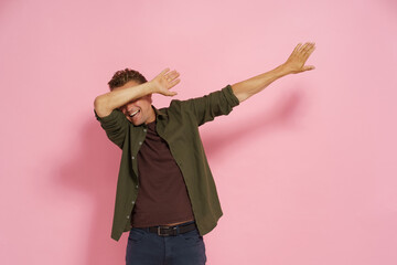 Joyful man performs the dab dance move in a studio with a plain pink background. Energetic expression captures playful mood of the moment, perfect for vibrant imagery.