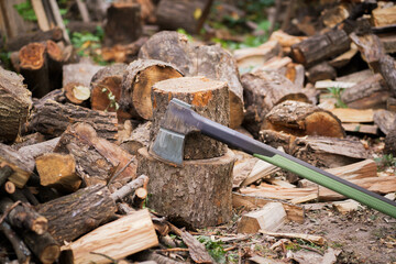 Rustic scene features an axe resting on a weathered tree stump. Surrounding pile of chopped firewood captures the essence of a utilitarian outdoor setting during the day.