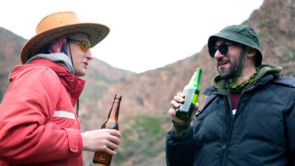 Two drunks are drinking beer in the mountains. Two male friends are chatting and holding a bottle of alcoholic beverage in their hands