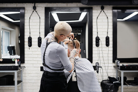 Horizontal rear view medium shot of unrecognizable professional female barber working in modern barbershop cutting hair of man