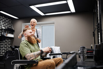 Horizontal shot of happy professional female barber finishing working on mans hairstyle in modern barbershop