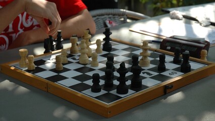 A child's hand moves a chess piece in a chess tournament. Several chess tables are lined up, a children's tournament. Chess pieces on a chess board.