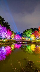 Naklejka premium Night scene of a park with colorful illuminated trees reflected in a pond