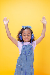 Cheerful, smiling Hispanic school-age girl with hearing aids making hand gestures,  on a yellow background.