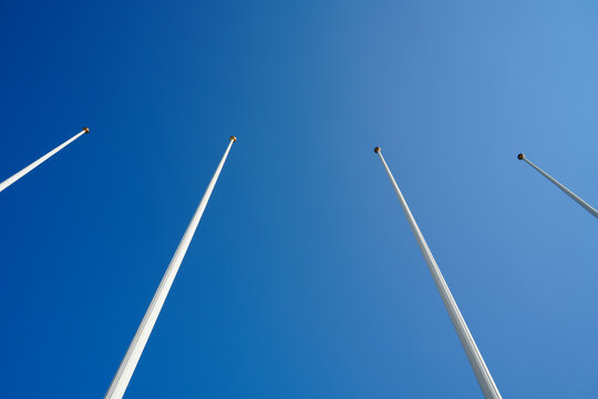 A low angle view of four empty flagpoles against a clear blue sky. The minimalist composition creates a powerful corporate background with copy space, symbolizing ambition, goals, and the future