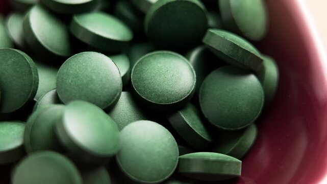 Green spirulina pills in red bowl. Nutrition detox supplement. Macro shot. Rotation