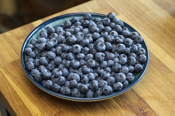 blueberries in a plate on the corner of a wooden table