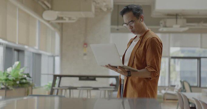 Senior Asian businessman wearing headset celebrates success during online meeting in modern co-working space. Remote work and business communication concept